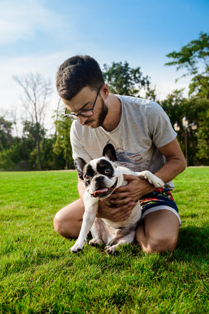 handsome man sitting with french bulldog on grass in park.